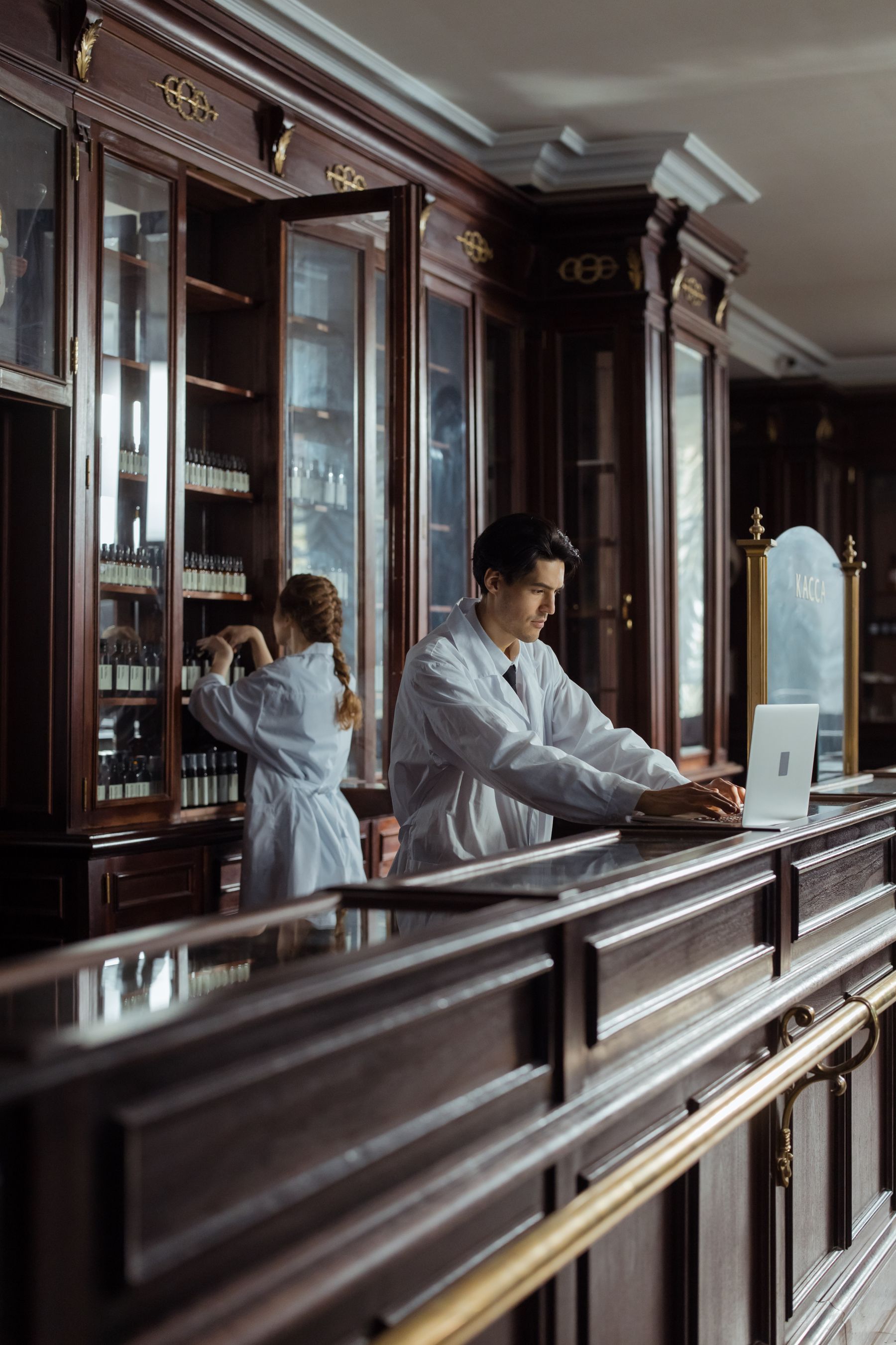 Pharmacy staff working with a laptop and medication cabinets.
